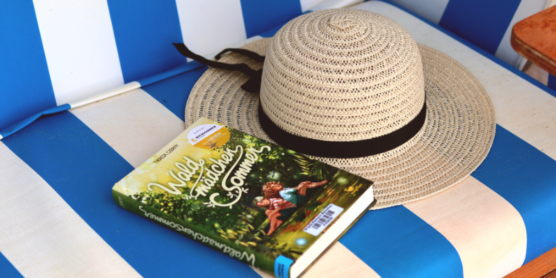 Zu sehen sind ein Strohhut und ein Buch, die in einem Strandkorb liegen.