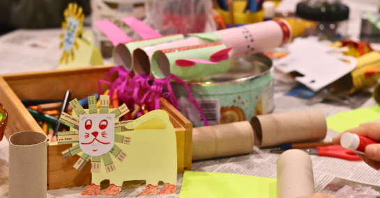 Zu sehen sind viele Bastelmaterialien, eine Löwe aus Papier, eine Rakete uns Toilettenpapierrollen und Zeitungsschnipsel.