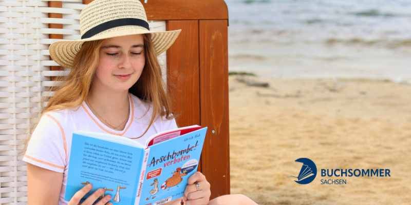 Zu sehen ist ein Mädchen am Strand, welches in einem Buch liest.