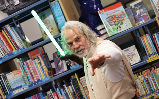 Star-Wars Cosplayer als Luke Skywalker in der Brigitte-Reimann-Stadtbibliothek Hoyerswerda mit grünem Lichtschwert vor einem Bücherregal