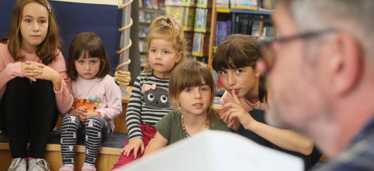 Kinder im Lesezelt der Bibliothek die einem Vorleser lauschen