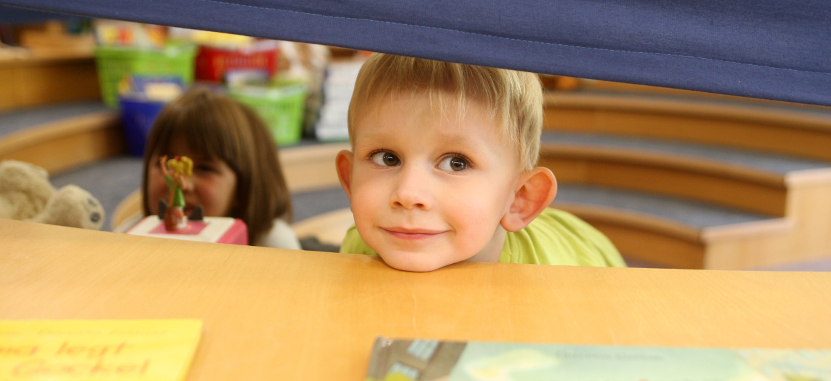 Kind, dass verschmitzt aus dem Lesezelt der Bibliothek schaut