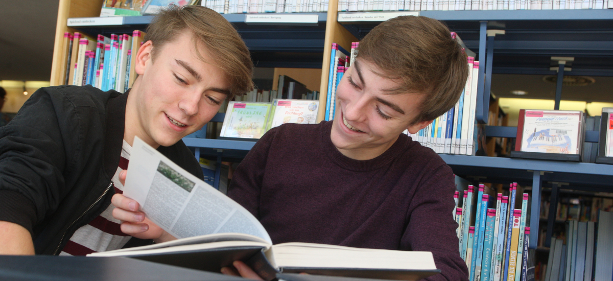 Zwei Jugendliche recherchieren in Büchern in der Bibliothek