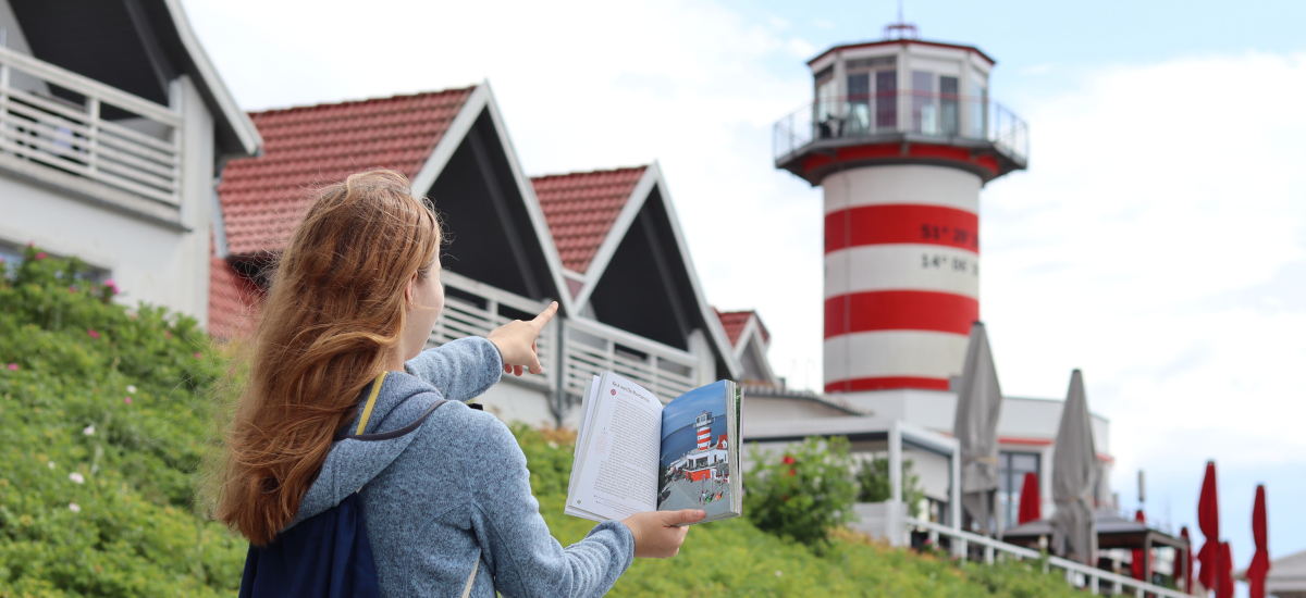 Eine junge Frau hält einen Reiseführer und zeigt auf dem Leuchtturm am Geierswalder See.