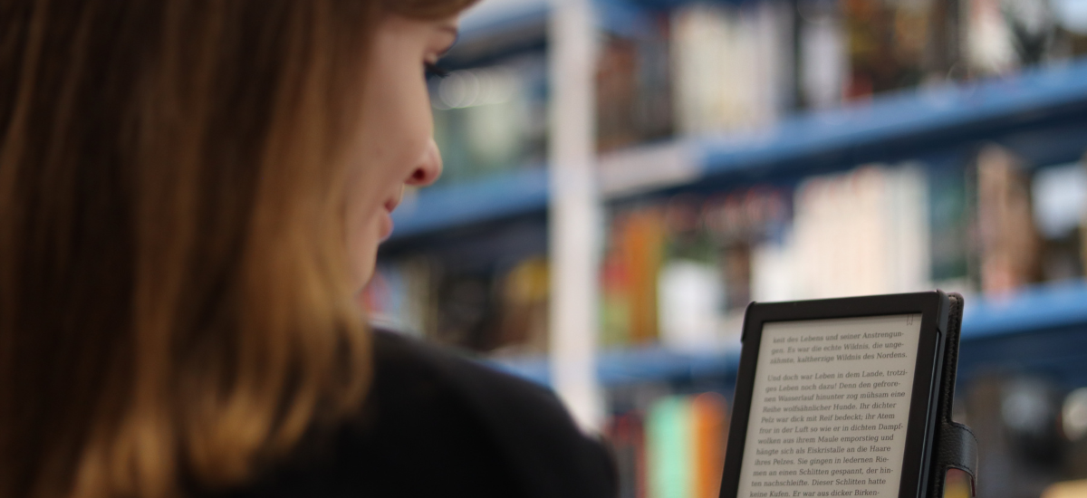 Junge Frau liest in der Bibliothek auf einem eBook-Reader.
