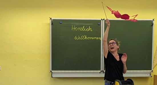 Frauke Angel bei einer Lesung zu ihrem Buch "Mama Mutsch und mein Geheimnis" wedelt in einem Klassenzimmer mit einem rosa BH