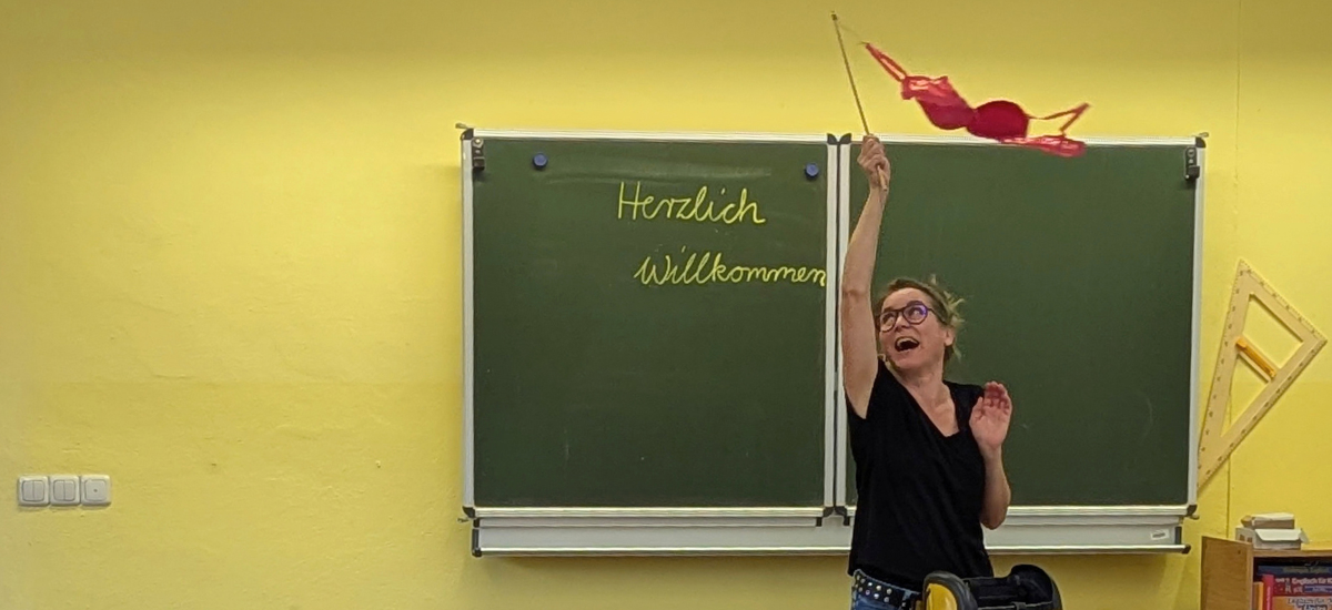 Frauke Angel bei einer Lesung zu ihrem Buch "Mama Mutsch und mein Geheimnis" wedelt in einem Klassenzimmer mit einem rosa BH